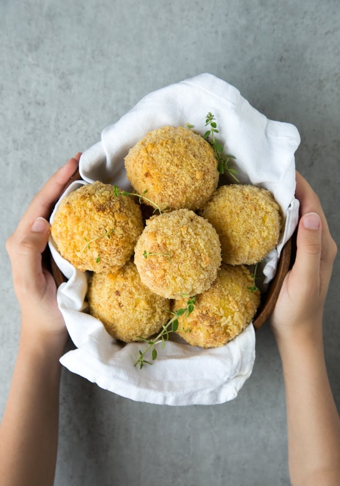 hands holding a bowl covered with a white napkin and filled with salmon and pea baked arancini balls