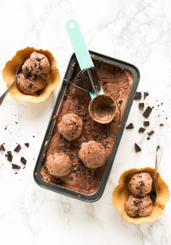chocolate ice cream in a container, next to two wafer cups filled with two balls of chocolate ice cream each.
