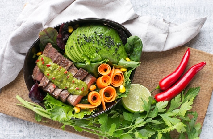 steak salad bowl with carrot, salad leaves,Avocado, steak topped with chimichurri sauce