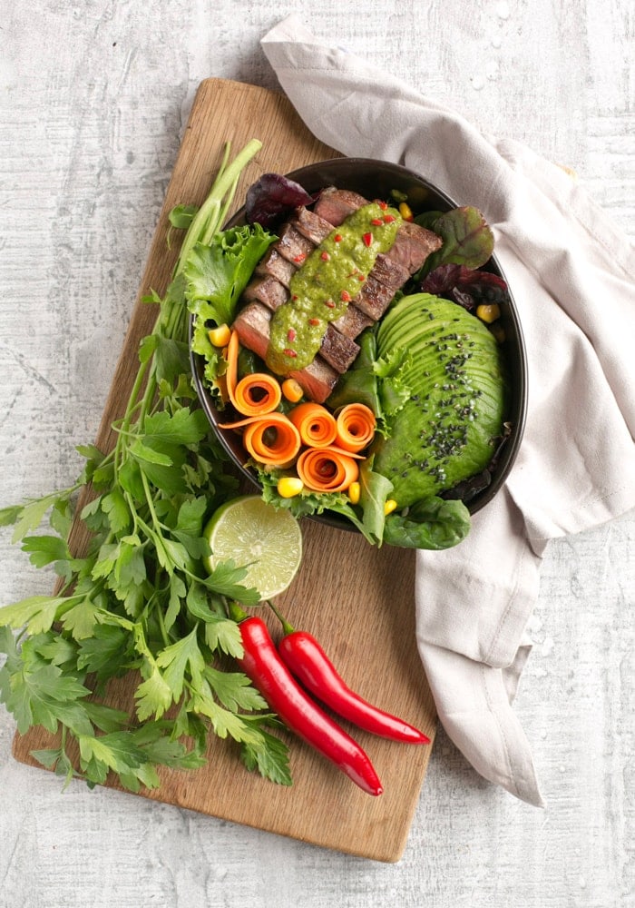 steak salad bowl with carrot, salad leaves, avocado, steak topped with chimichurri sauce