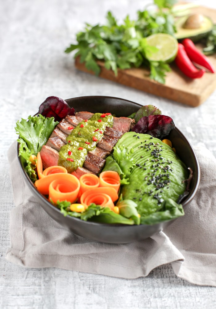 steak salad bowl with carrot, salad leaves, steak topped with chimichurri sauce