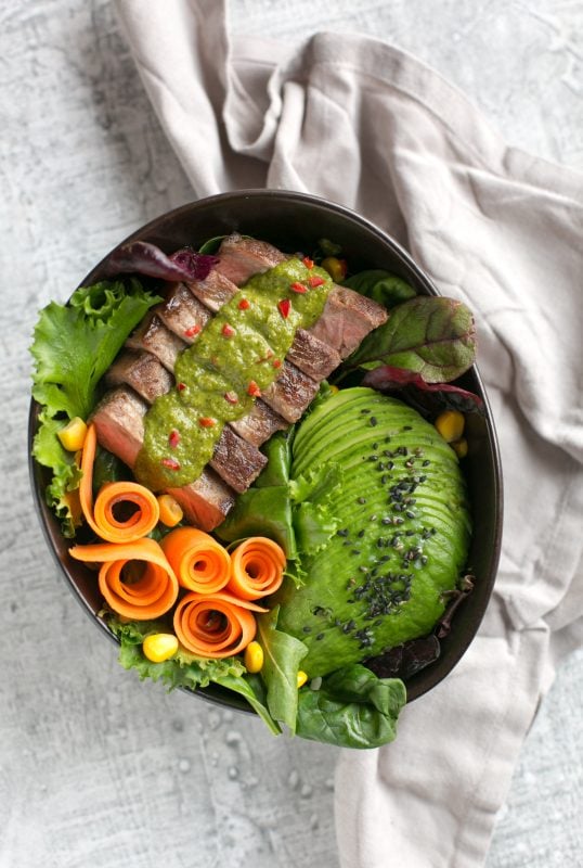 steak salad bowl with carrot, salad leaves, avocado, steak topped with chimichurri sauce