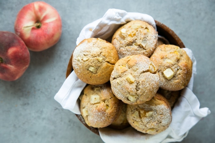 peach muffins in a bowl and 2 peaches on the background