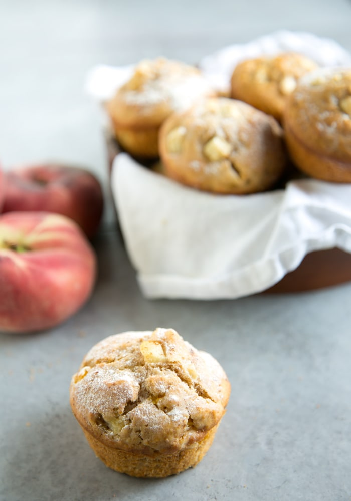 peach muffin on focus and peach muffins in a bowl on the background, 2 peaches in the background