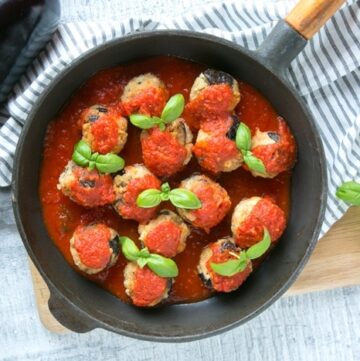 Vegetarian Aubergine Meatballs in pan over striped napkin and wood chopping board, basil leaves on the top right corner.