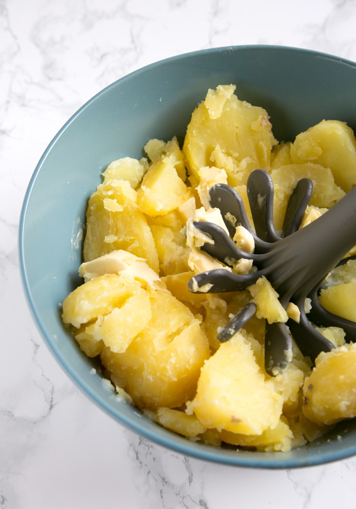 recipe step 1: boiled potatoes in a bowl, with softened butter and potato masher