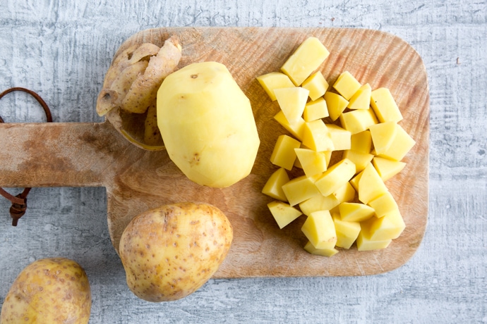 recipe step 1: chopped potatoes, peeled potato and unpeeled potatoes on wood board