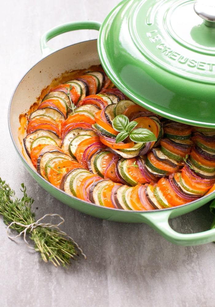 Easy Ratatouille in a large green cast iron shallow pan with lid on the side, bunch of thyme sprigs on the left side and a green napkin on the top right side.