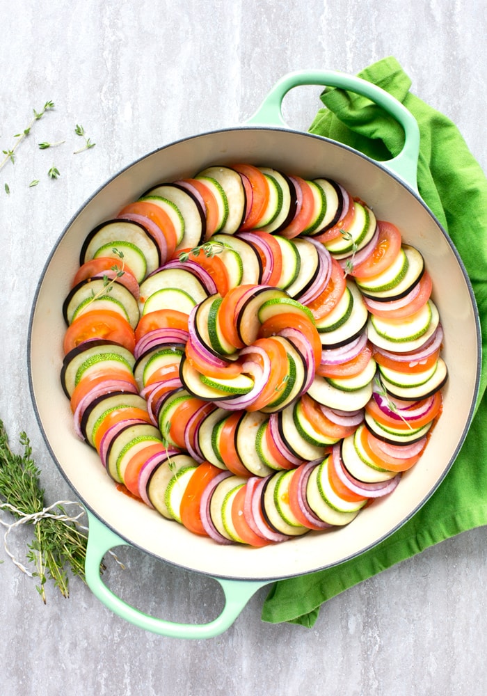 Raw Easy Ratatouille in a large green cast iron shallow pan, bunch of thyme sprigs on the left side and a green napkin on the top right side.