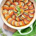 Ratatouille in a large green cast iron shallow pan, bunch of thyme sprigs on the left side and a green napkin on the top right side.