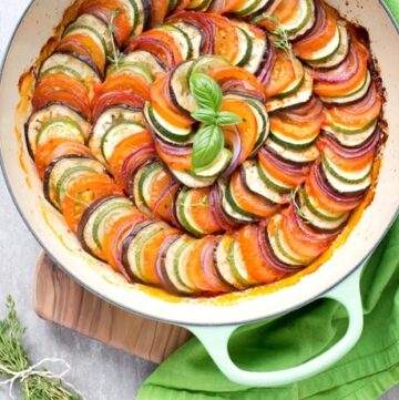 Ratatouille in a large green cast iron shallow pan, bunch of thyme sprigs on the left side and a green napkin on the top right side.