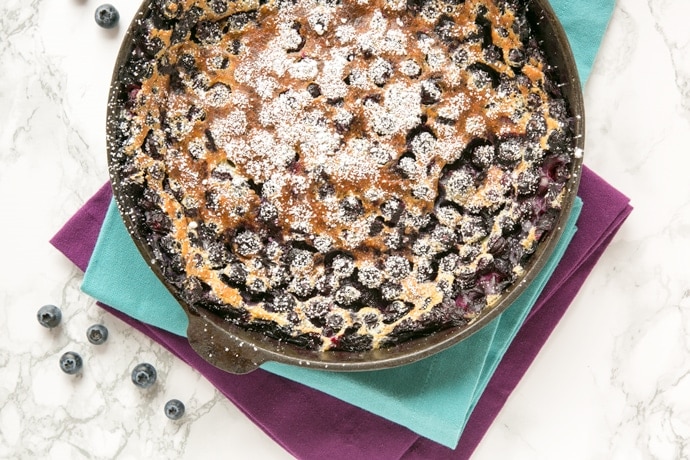 french blueberry clafoutis in a cast-iron skillet over two cloth napkins.