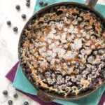 french blueberry clafoutis in a cast-iron skillet over two cloth napkins.