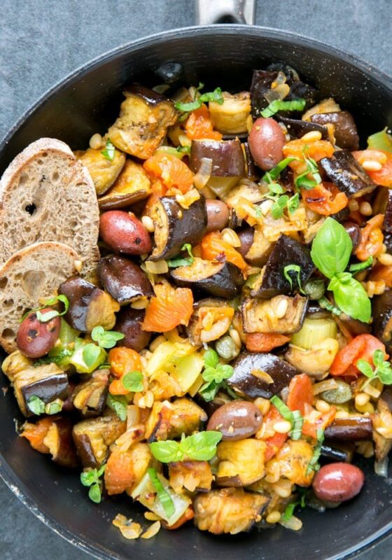 eggplant caponata in a skillet served with crusty bread slices