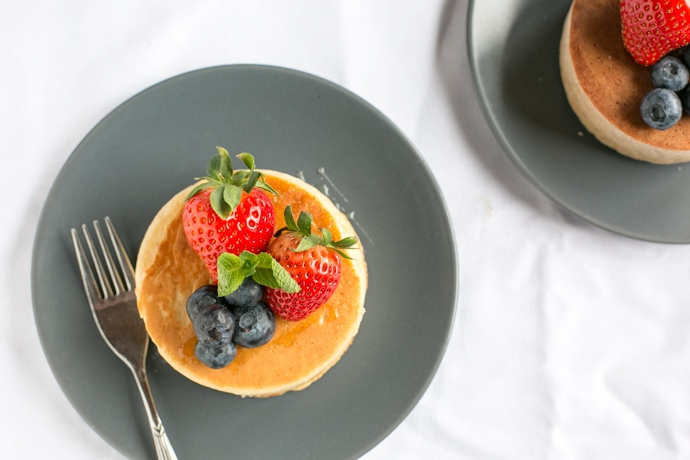 Japanese pancakes topped with strawberries and blueberries and fork next to it, on grey plate and white tablecloth