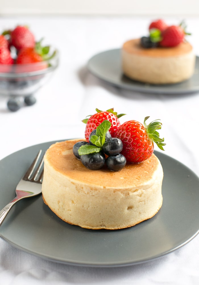 Japanese pancakes topped with strawberries and blueberries and fork next to it, on grey plate and white tablecloth