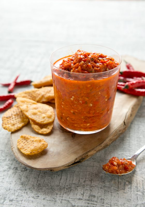 peri peri sauce in a large glass and in a spoon next ot it, served with tortilla chips on the side