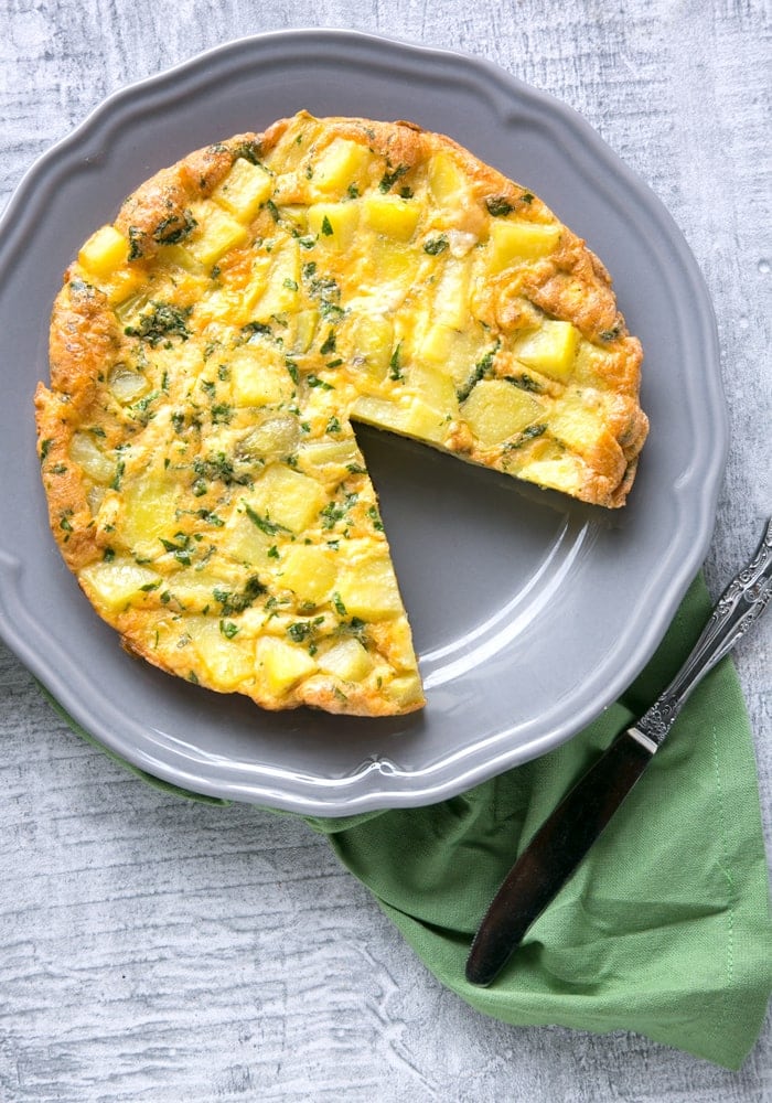 Classic Italian Potato Frittata on a grey serving plate and knife on green napkin on the side.