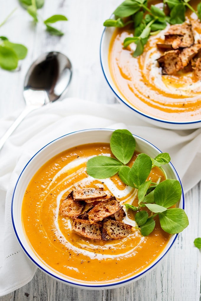 Baked sweet potato and carrot soup with cheddar potato skin croutons in two bowls, white napkin, and spoon in the background