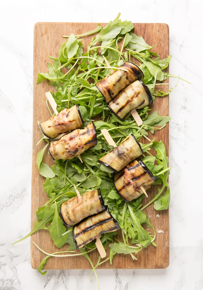 eggplant roll-ups over a bed of rocket leaves on a wood board
