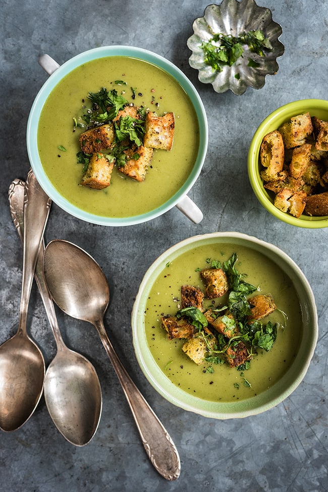 spinach coconut and zucchini soup in two bowls, next to 3 spoons.