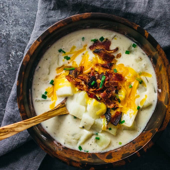 Creamy Potato Soup with Bacon and Cheddar in wood bowl with wood spoon and grey napkin in the background