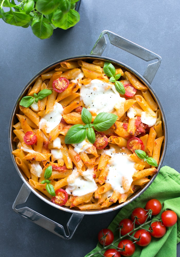 caprese pasta bake in a large baking pan, topped with mozzarella and basil leaves