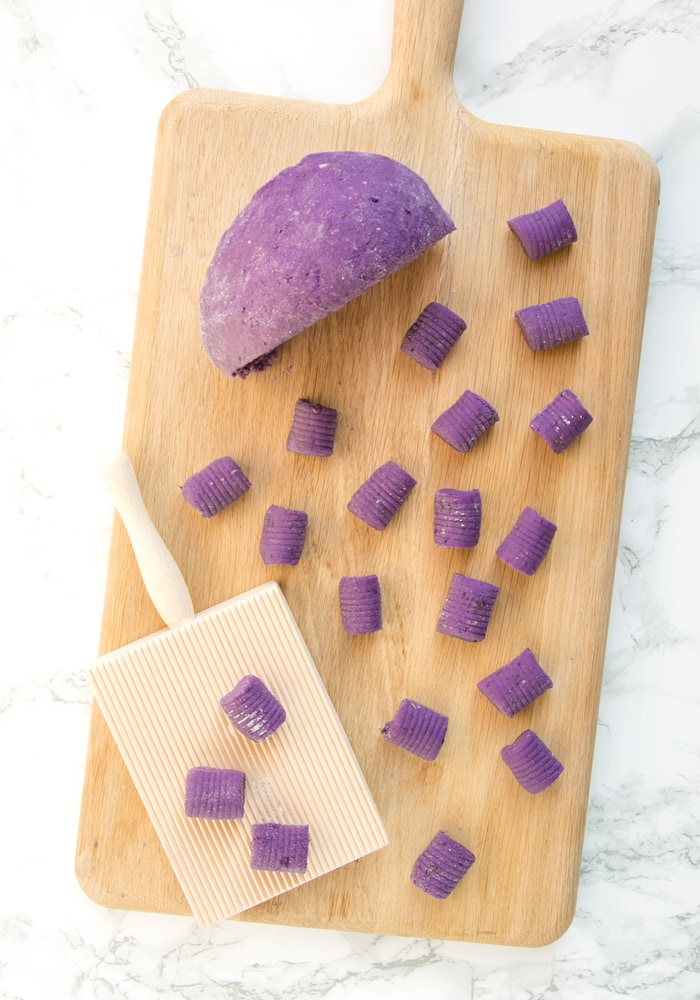 Homemade purple potato gnocchi on a wood board, next to the dough and gnocchi wood board.