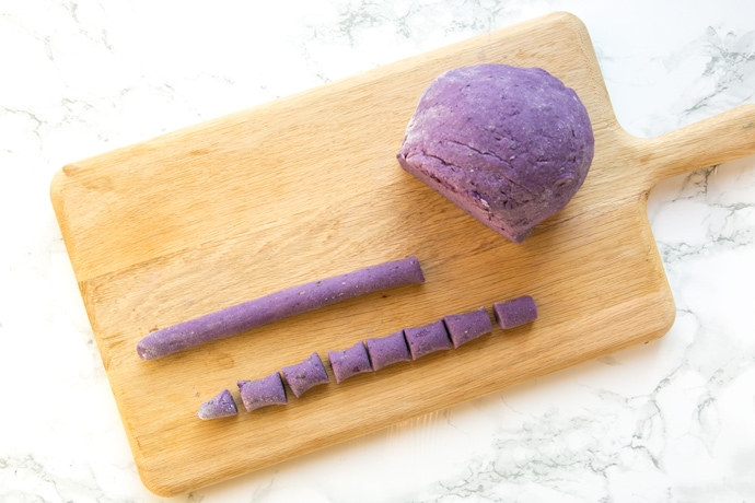 purple gnocchi dough next to a string of dough and another string cut into tiny rectangulars.