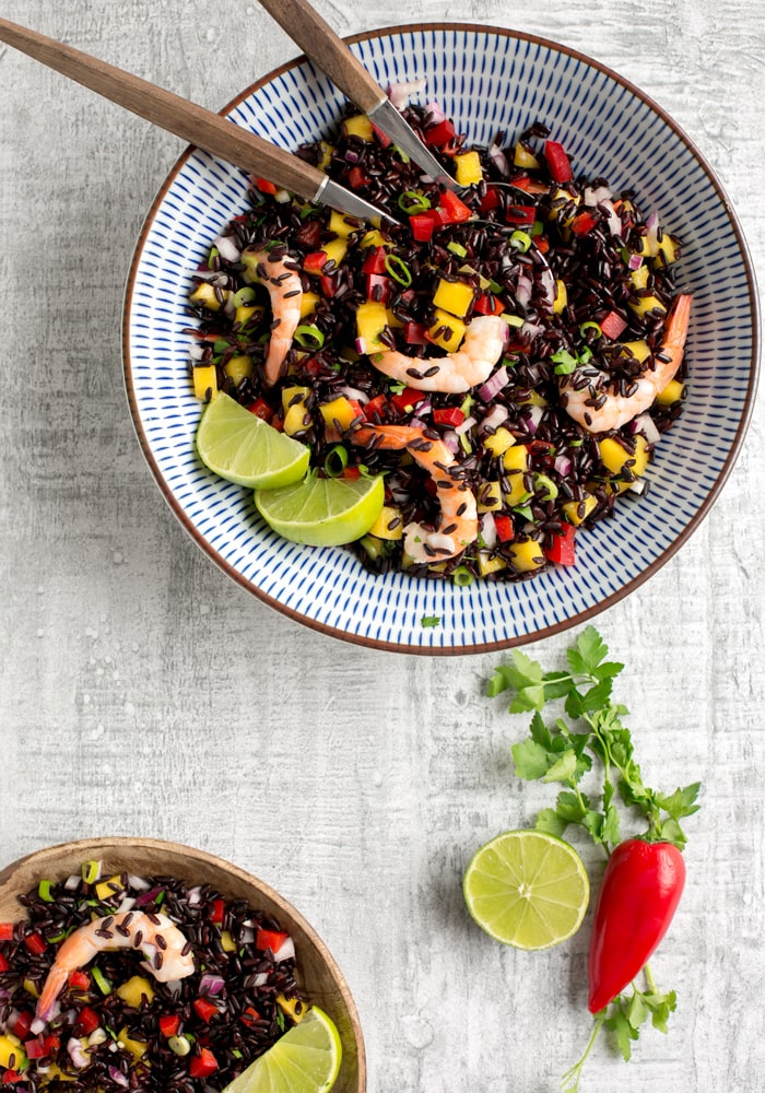 venere black rice salad with shrimps and mango salsa in a bowl, with lime and chili pepper on side