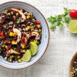 venere black rice salad with shrimps and mango salsa in a bowl, with lime and chili pepper on side