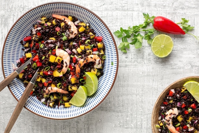 venere black rice salad with shrimps and mango salsa in a bowl, with lime and chili pepper on side