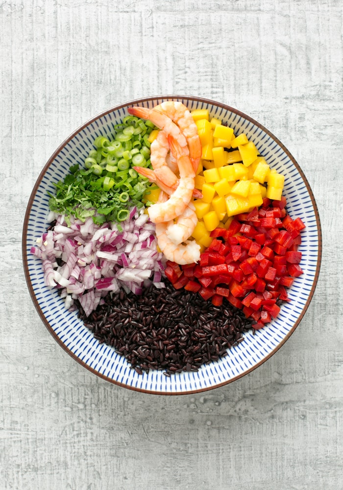 venere black rice salad with shrimps and mango, pepper, red onion, spring onion, shrimps in a bowl