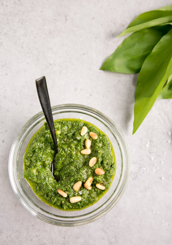 wild garlic pesto topped with pine nuts in glass bowl, wild garlic in the background