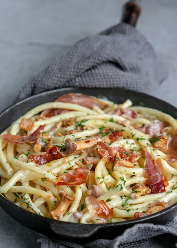 Creamy Pasta with Chanterelle Mushrooms and Crispy Prosciutto in cast iron skillet with a grey towel covering the handle