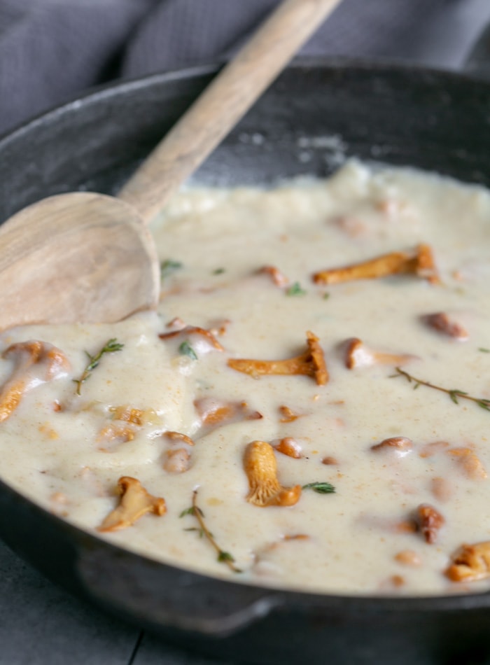 pasta with chanterelle preparation shot, mushroom sauce in a iron skillet and a wood spoon on the side.