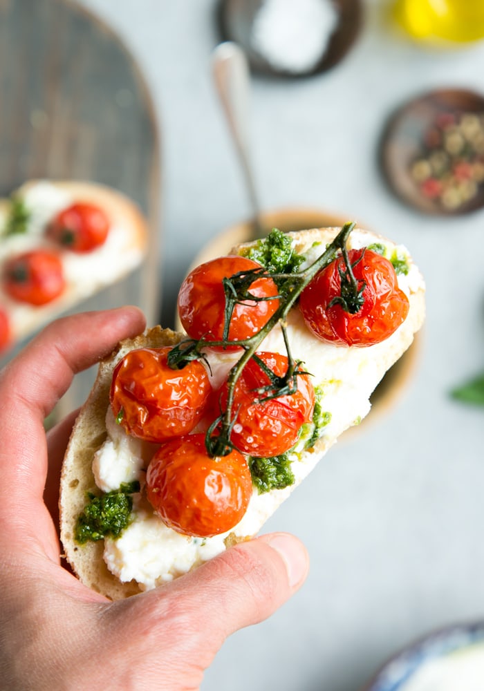 hand holding cherry tomato confit bruschetta with ricotta and basil pesto