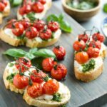 confit tomato bruschetta with ricotta and basil pesto over a wood board