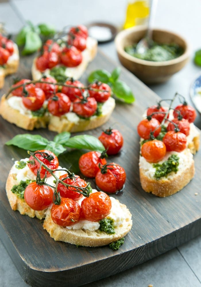 confit tomato bruschetta with ricotta and basil pesto over a wood board