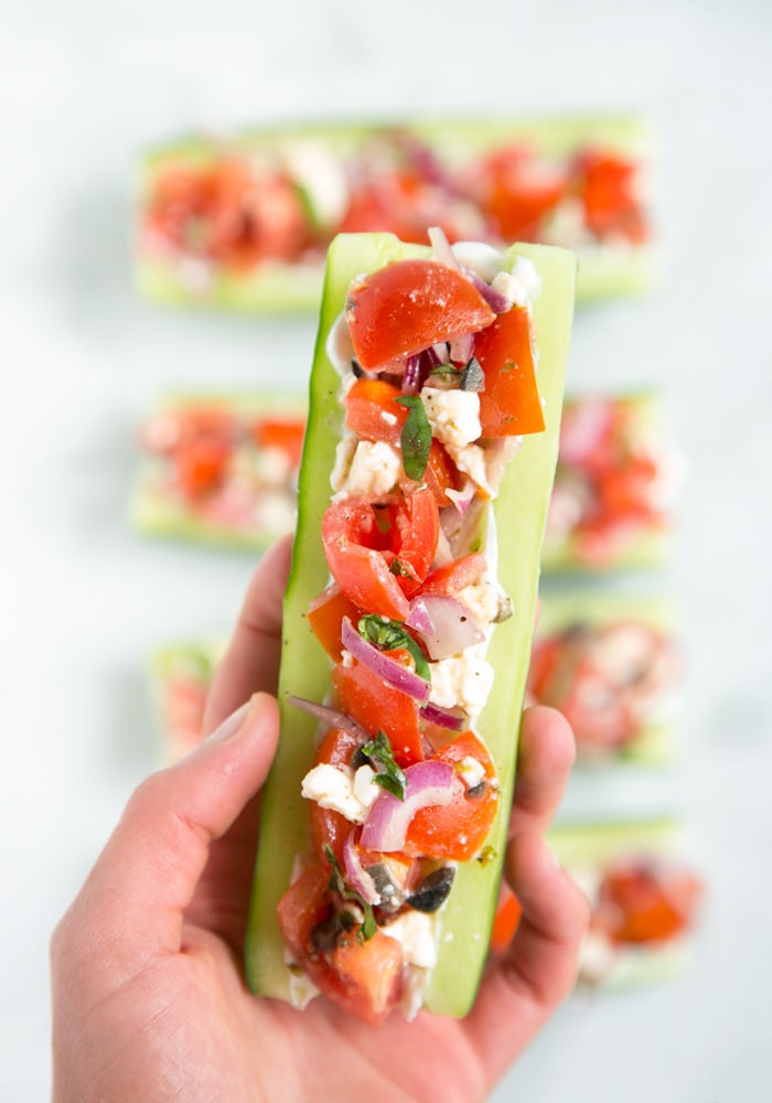 hand holding cucumber boat with greek salad filling