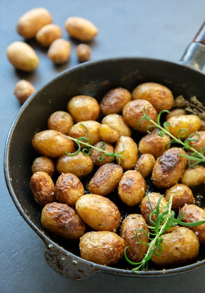 Italian pan roasted new potatoes with rosemary in skillet, raw potatoes in the background