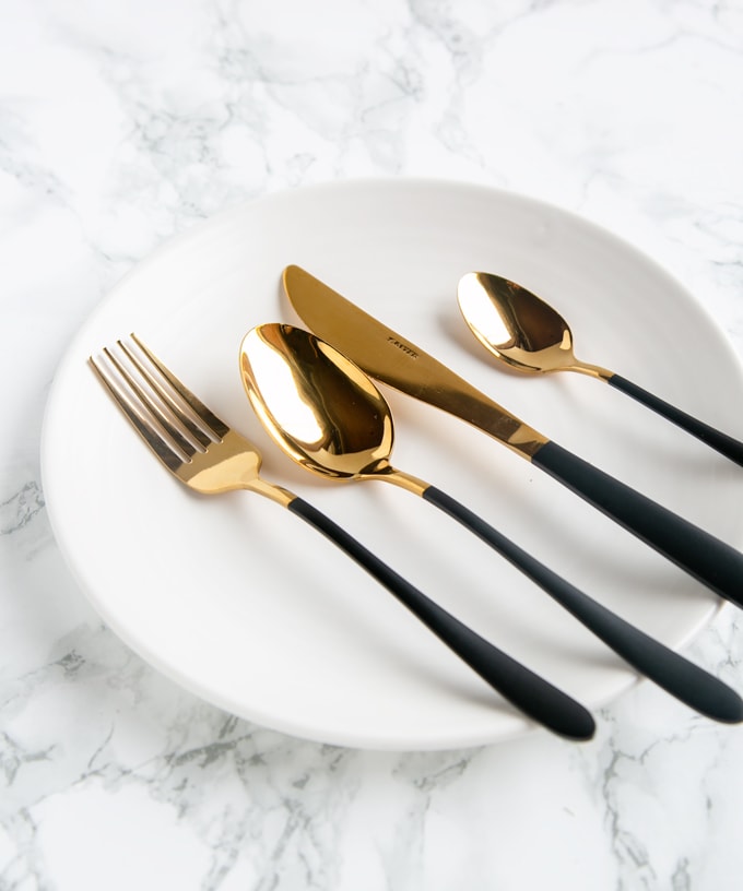 Foodie Gift Guide: Black and Gold cutlery set on a white plate and marble background