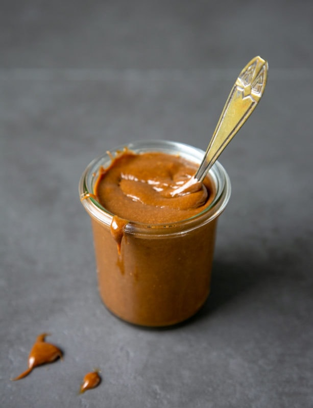 homemade dulce de leche in a small glass jar with teaspoon inside