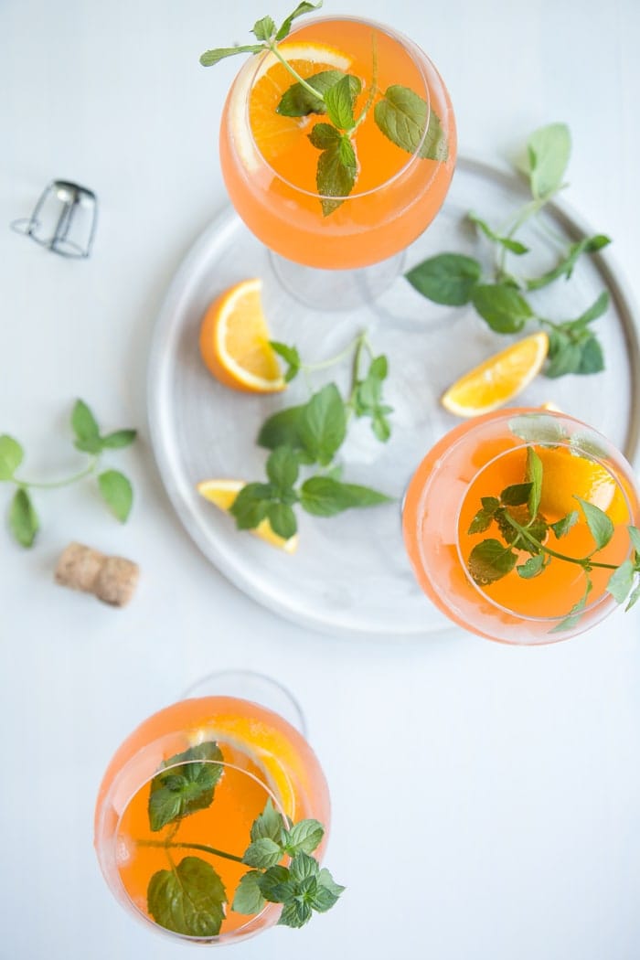 orange spritz cocktail in three wine glasses decorated with orange slices and mint leaves