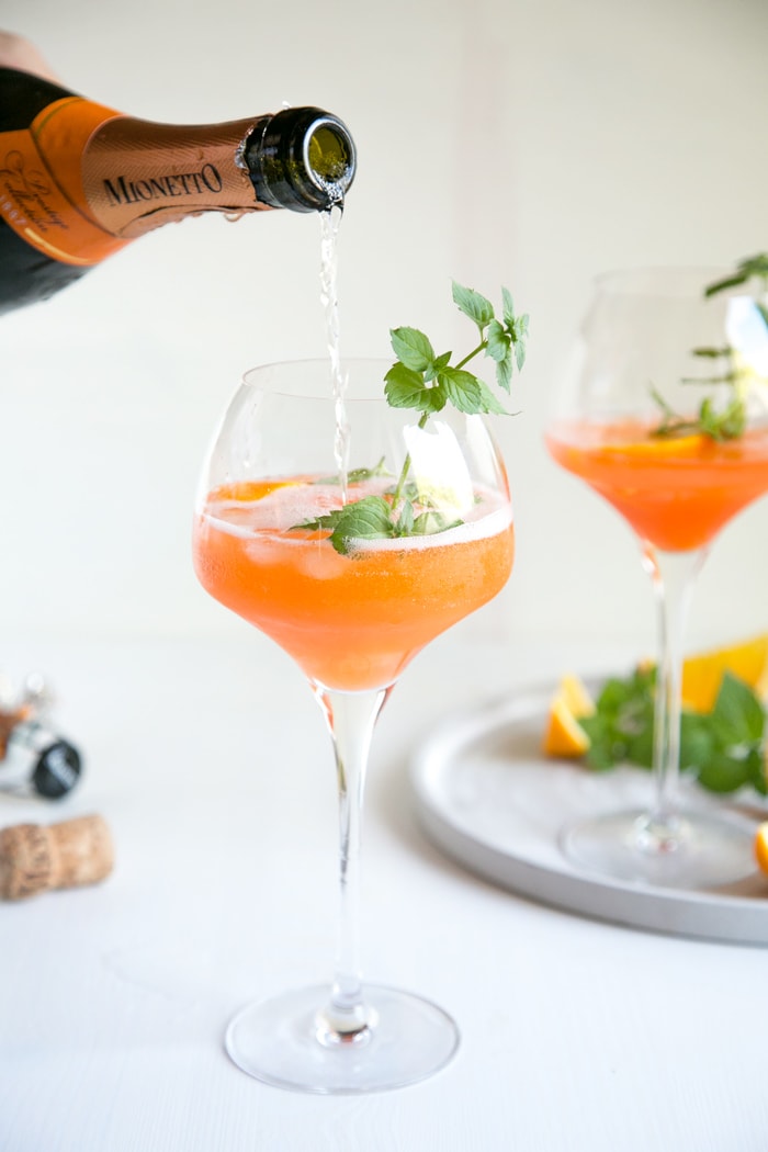 prosecco pouring from bottle into orange spritz glass garnished with mint leaves