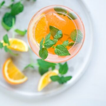 italian orange spritz in large wine glasse decorated with orange slice and fresh mint leaves
