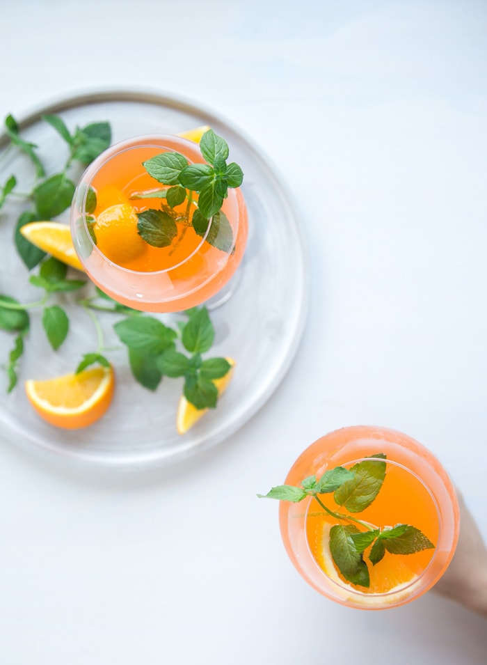 orange spritz in two glasses, one held by hand