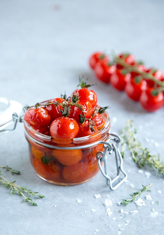 tomato confit in a jar, cherry tomatoes on the vine, thyme leaves and sea salt flakes in the background