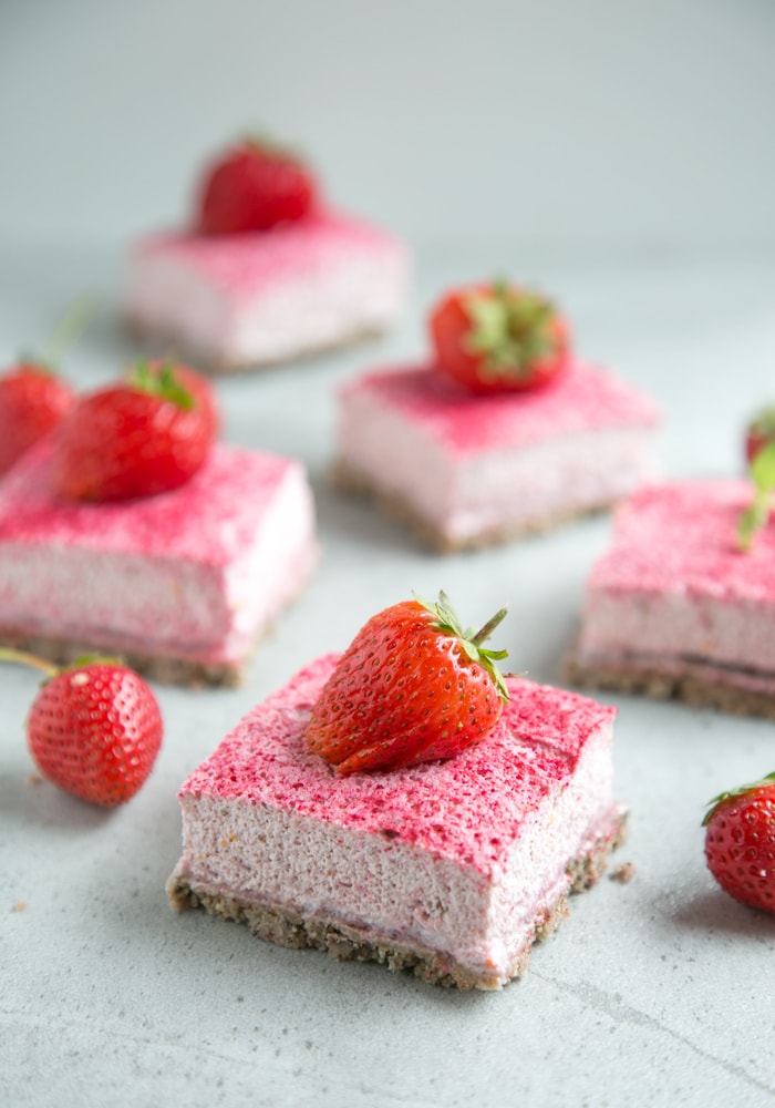 close up of one strawberry cheesecake bar, more bars and fresh strawberries out of focus on the background