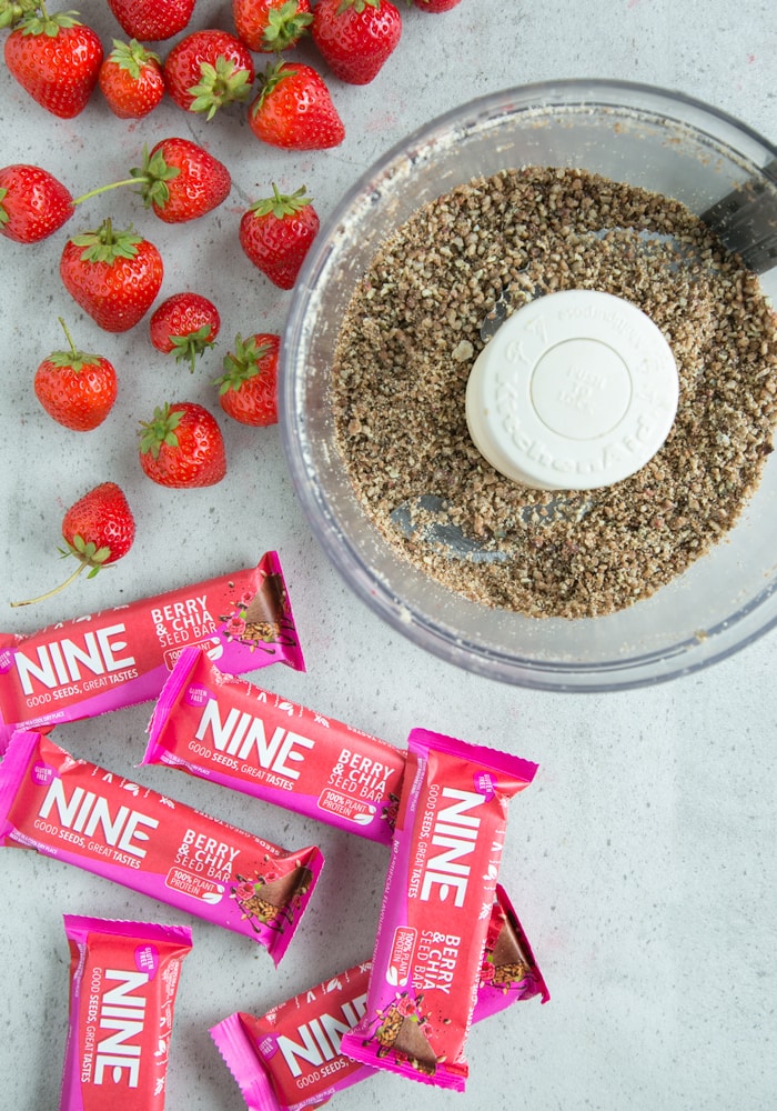 strawberry cheesecake bars in food processor, next to fresh strawberries and NINE bars